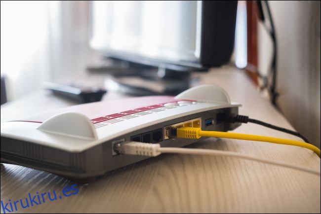 Cables conectados a la parte posterior de un módem que se encuentra en un escritorio junto a una computadora.