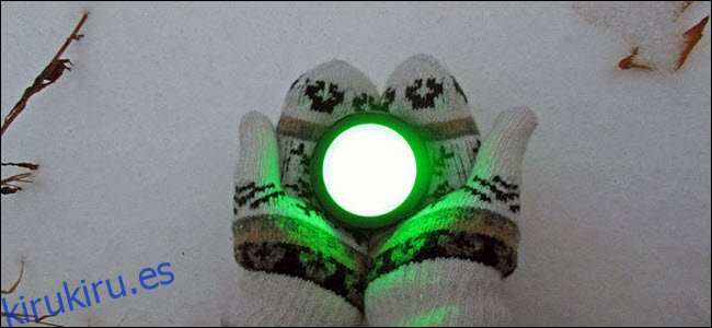 Un par de manos enguantadas sosteniendo un botón de eco que brilla intensamente en verde sobre la nieve.