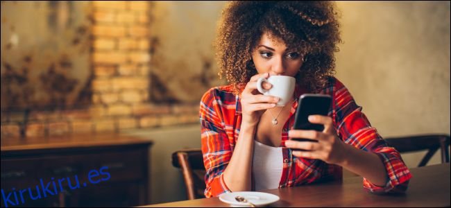 Una mujer sentada en una mesa mirando un teléfono inteligente y tomando café.