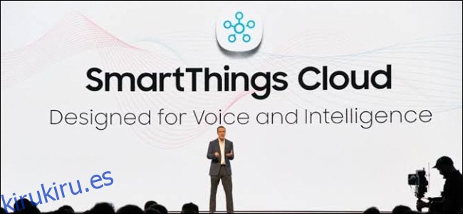 Un hombre en un escenario frente a un enorme telón de fondo de Samsung SmartThings Cloud.