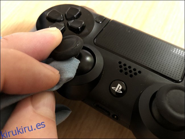 Una mano limpiando un stick analógico con un paño en un controlador DualShock 4.
