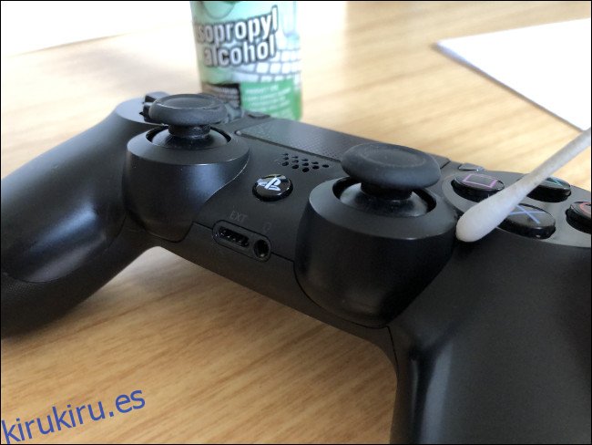 Un controlador DualShock 4 con un hisopo encima junto a una botella de alcohol isopropílico.