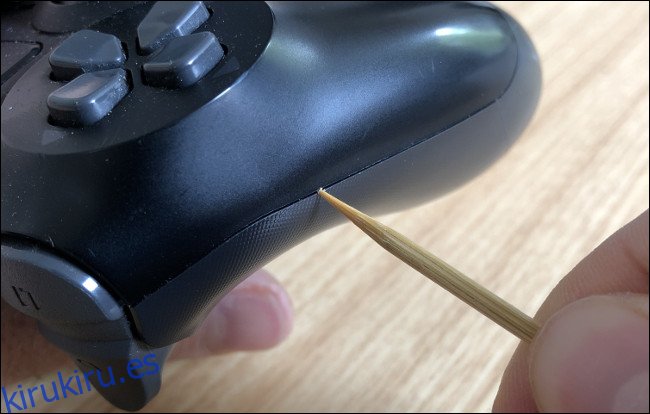Una mano limpiando una hendidura en el lateral de un DualShock 4 con un palillo.