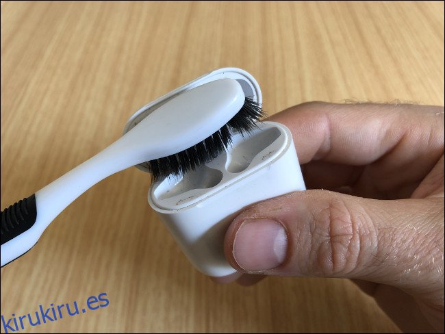 Una mano sosteniendo un estuche de Apple AirPods y limpiándolo con un cepillo de dientes.