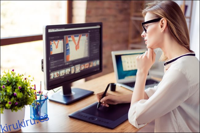 Una mujer mirando la pantalla de una computadora mientras dibuja en una tableta digital.