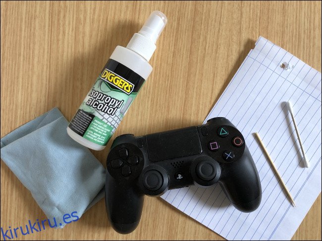 Un controlador DualShock 4 colocado encima de un trozo de papel junto a un palillo, un hisopo, una botella de spray de alcohol isopropílico y un paño. 