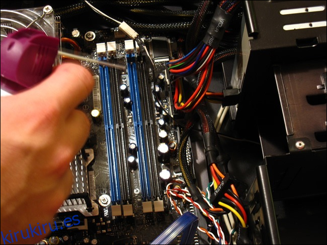 Una mano sosteniendo una lata de aire comprimido sobre una caja de computadora abierta. 