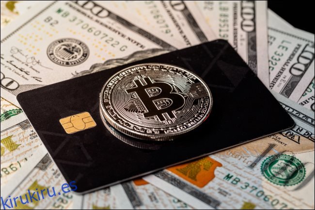 Un token físico de Bitcoin encima de una tarjeta de crédito sobre billetes de $ 100.