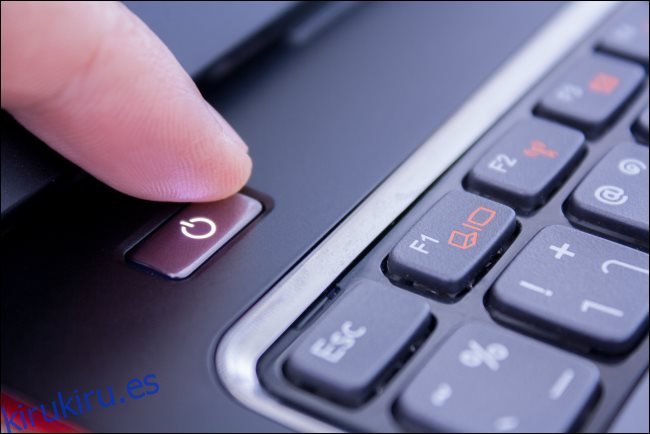 Un dedo presionando el botón de encendido de una computadora portátil para apagarla.