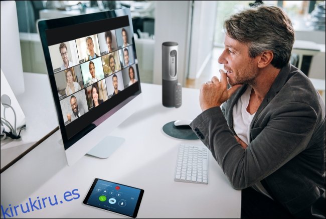 Un hombre en una reunión de Zoom en su Mac con los participantes en la vista de galería en el monitor. 