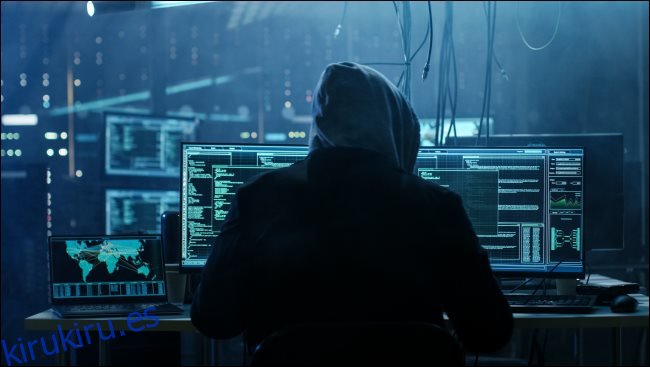 Un hacker en la sombra con una sudadera con capucha sentado frente a una computadora.