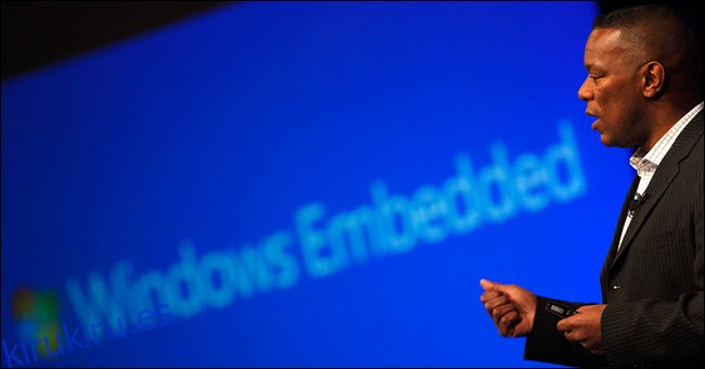 Hombre hablando frente al logo de Windows Embedded.