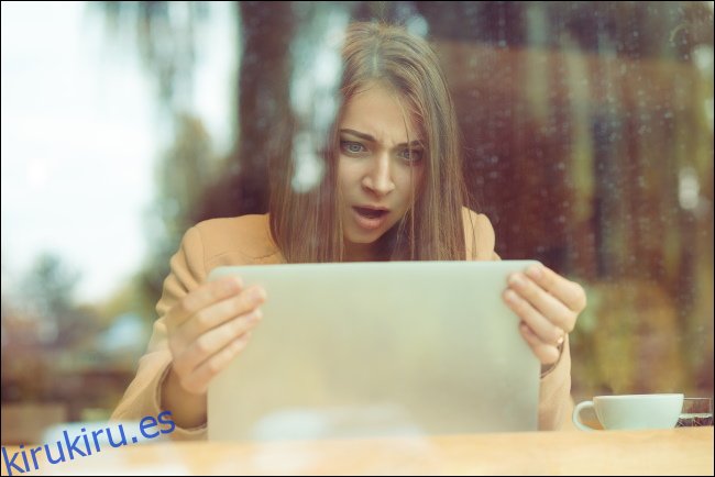 Una mujer sorprendida sosteniendo la pantalla de su computadora portátil.