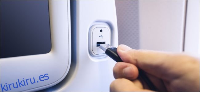 Una mano que conecta un cable USB a un puerto de carga en la parte posterior del asiento de un avión.