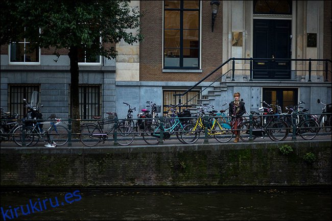 Una mujer de pie sobre un puente detrás de una línea de bicicletas estacionadas.